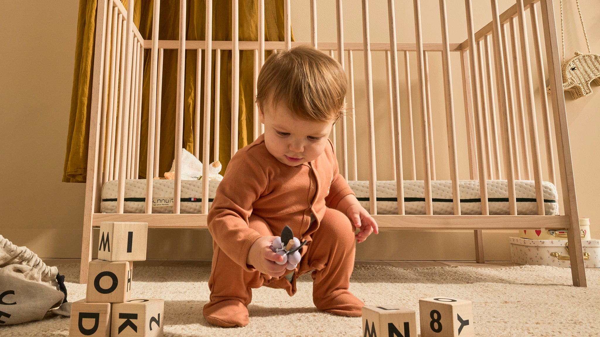 Bébé jouant dans sa chambre avec un lit à barreaux et un matelas Bonnuit visibles en arrière-plan