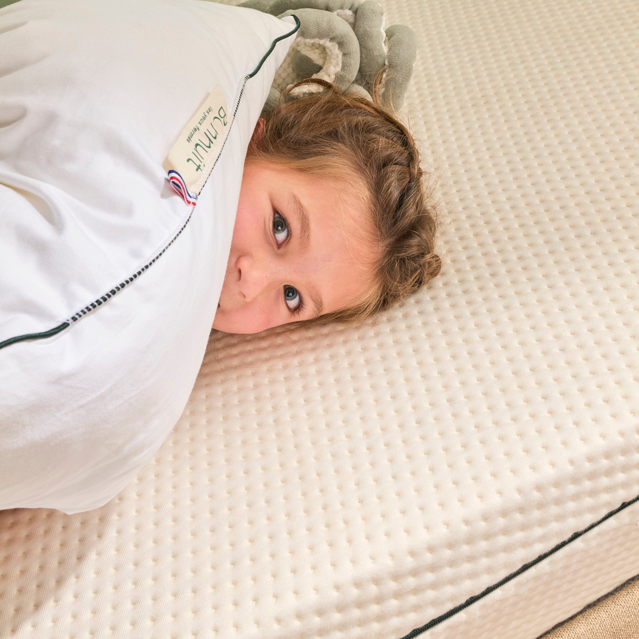 Enfant souriant allongé sur un matelas housse bambou et un oreiller à mémoire de forme Bonnuit, étiquette et BBR visibles