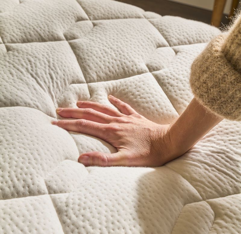 Zoom sur le plateau du matelas Le Merveilleux Bonnuit avec une main posée dessus, illustrant le confort de l’accueil en latex naturel