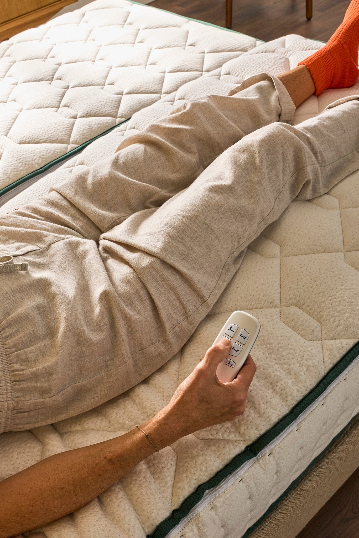 Zoom sur la télécommande du sommier électrique Divin et les jambes du modèle sur un matelas Original Bonnuit