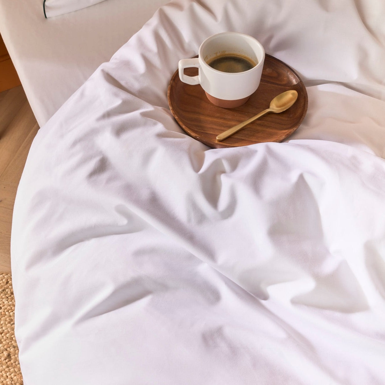Tasse de café posée sur une couette blanche en percale avec liseré vert, ambiance douce et calme