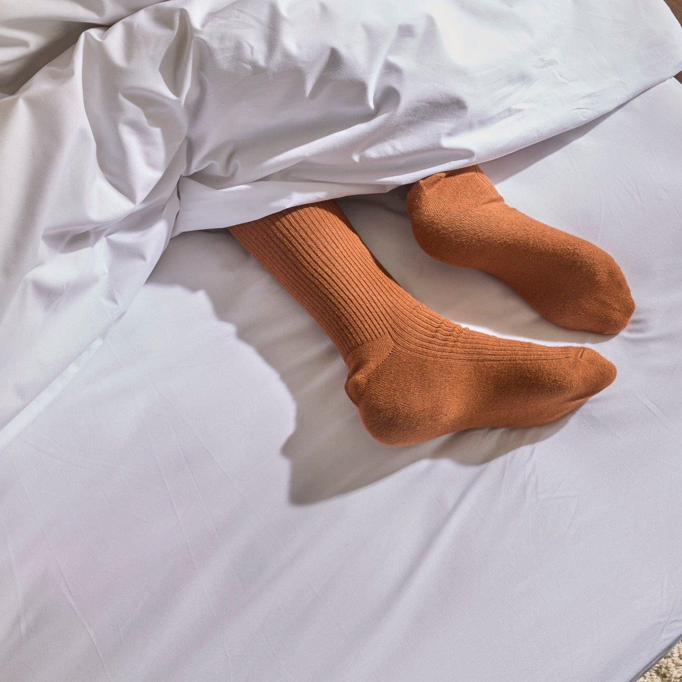 Pieds en chaussettes sur un lit avec linge de lit en percale blanche à liseré vert, ambiance décontractée