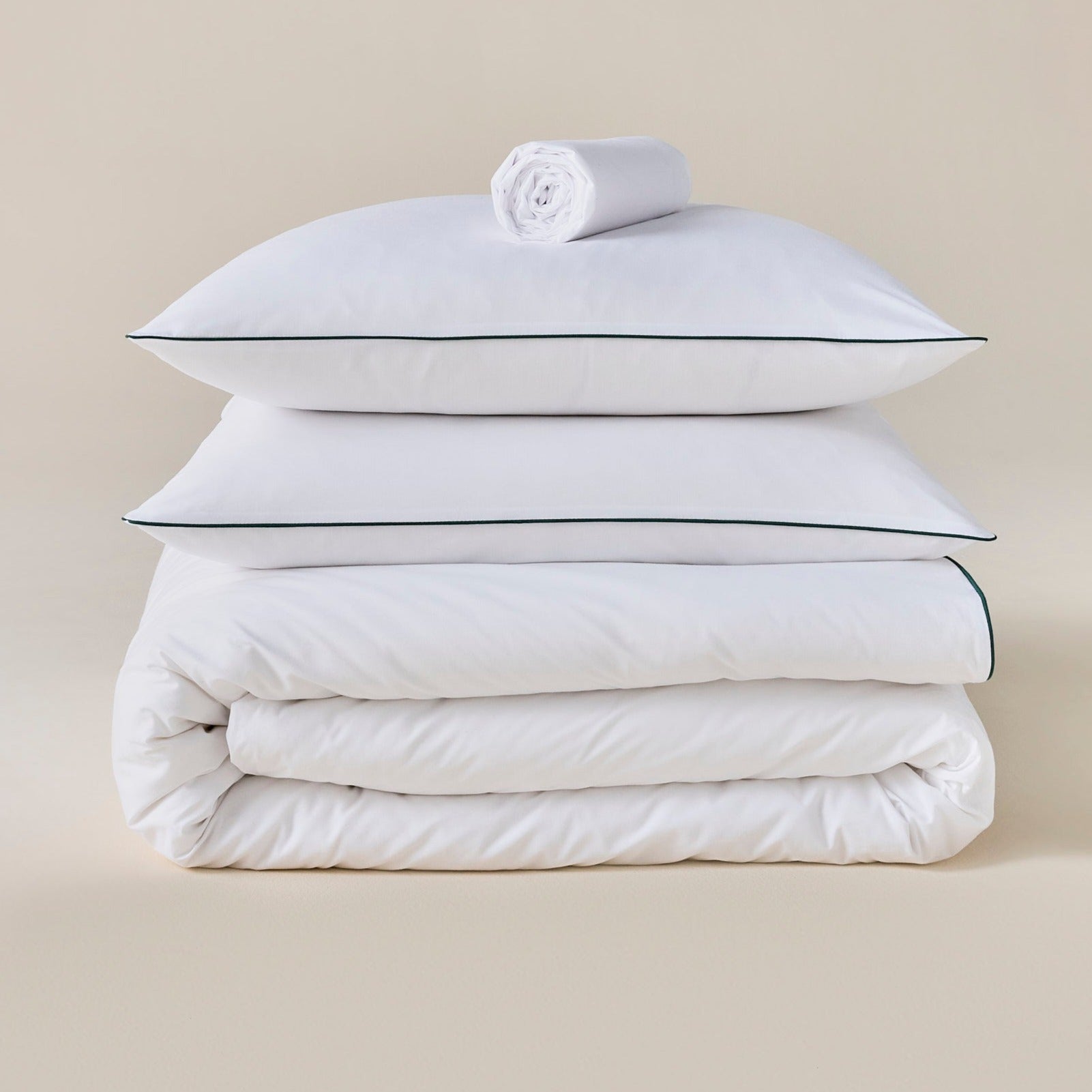 Parure de lit en percale blanche avec liseré vert, oreillers posés sur une couette, linge roulé au-dessus