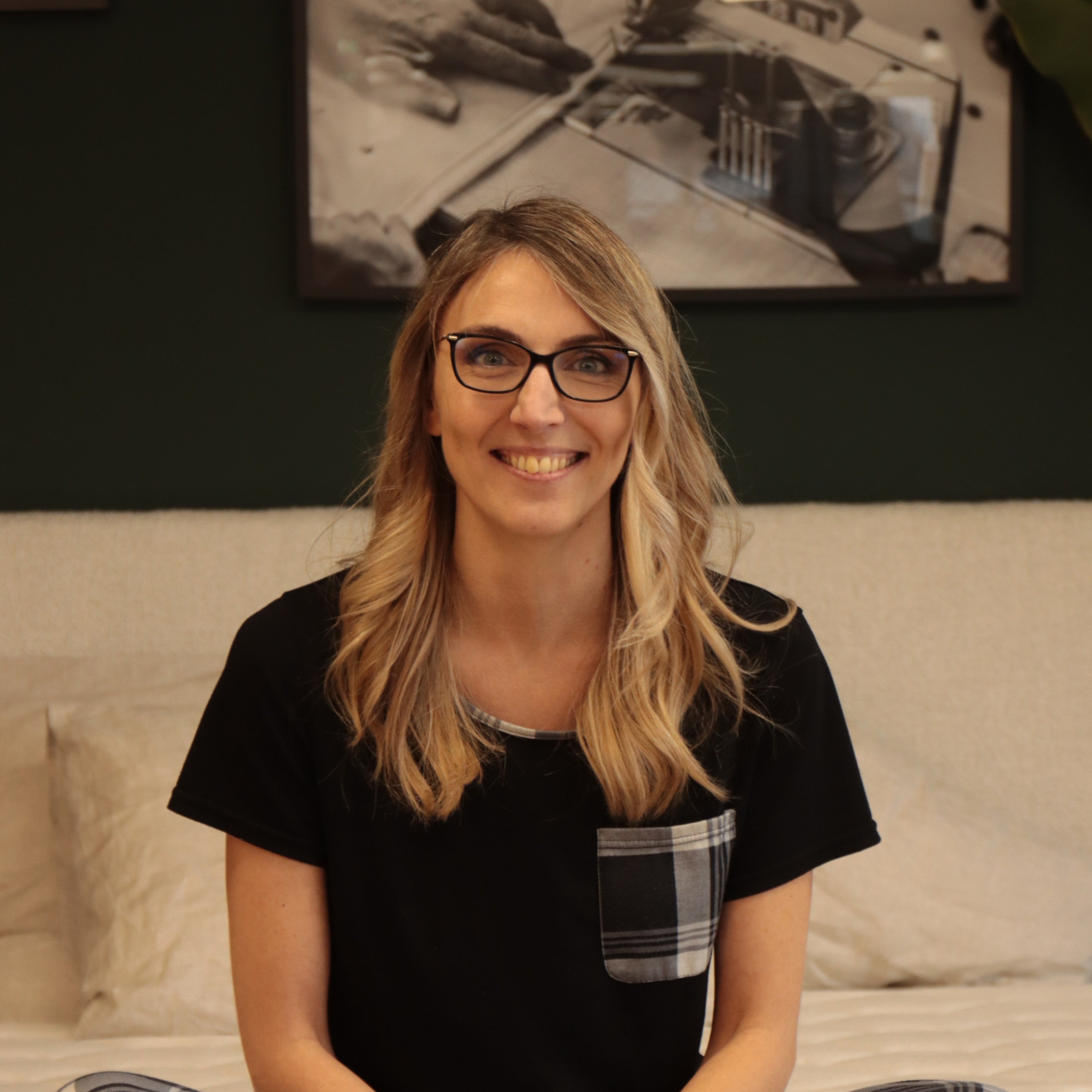 Amélie, commerciale Bonnuit, assise en pyjama sur un lit, affichant un large sourire et une posture détendue