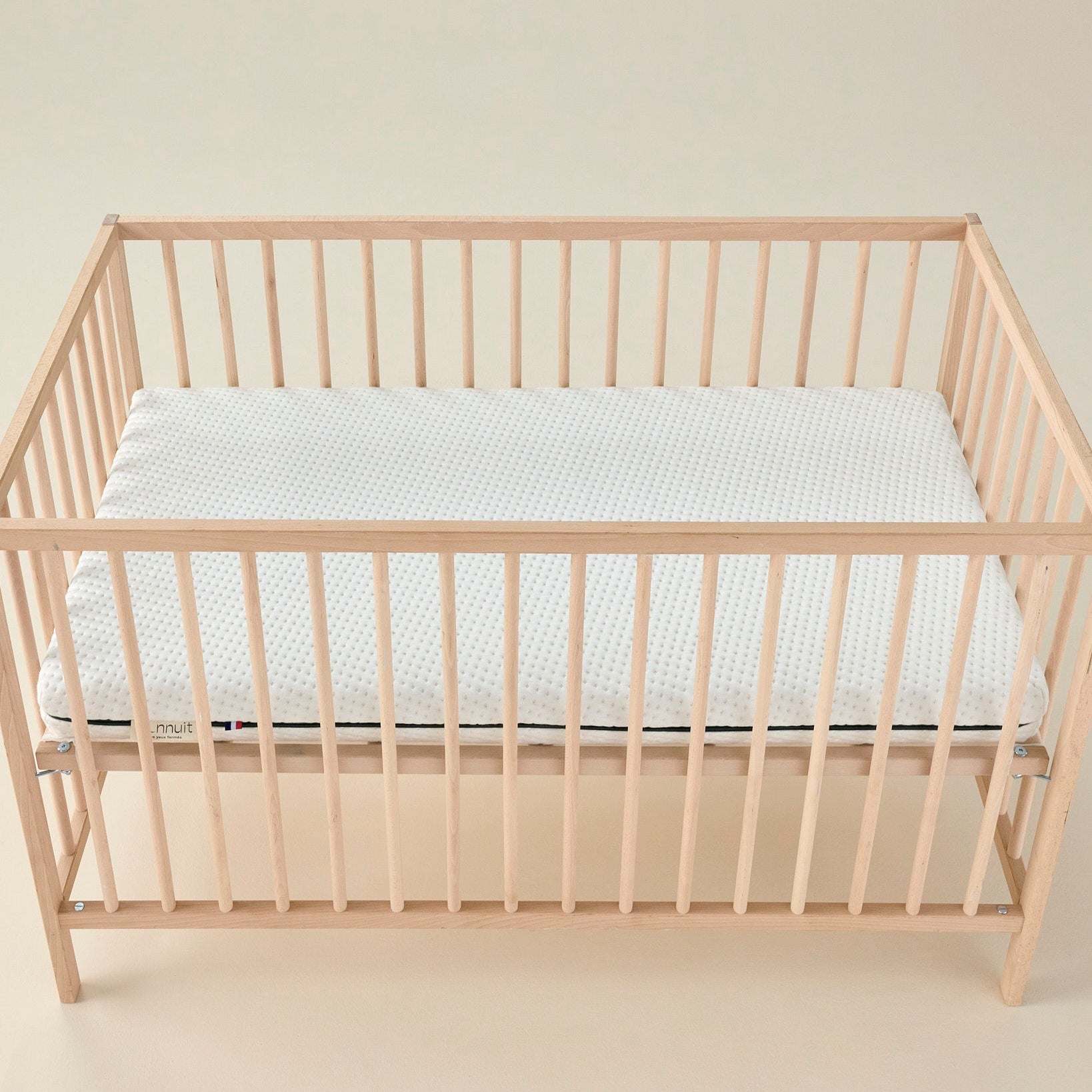 Matelas bébé Mini Mousse vu de côté, housse claire, liseré bleu et étiquette discrète