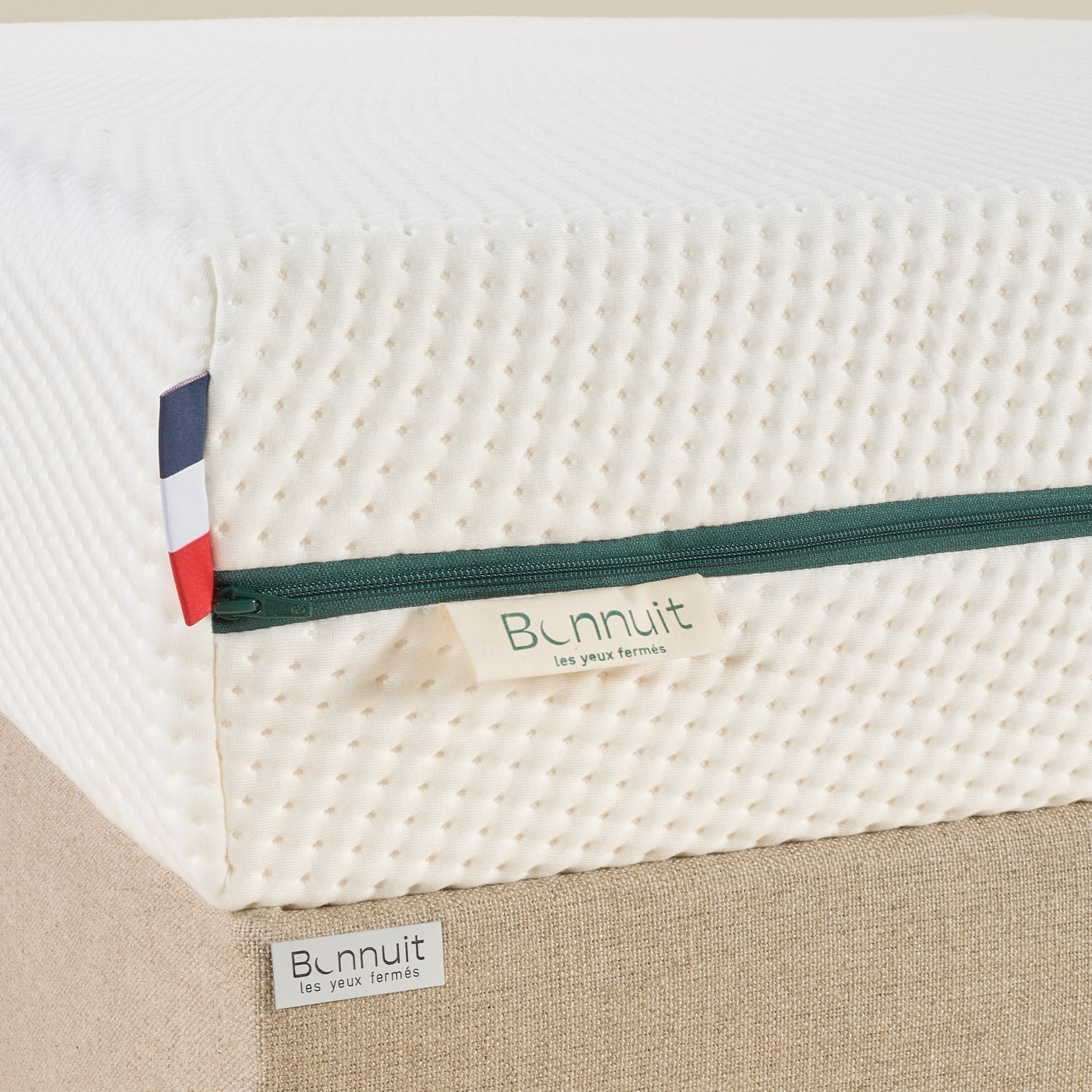 Zoom sur le coin du matelas L’Essentiel Bonnuit avec housse blanche, fermeture verte, logo brodé sur lin et drapeau français