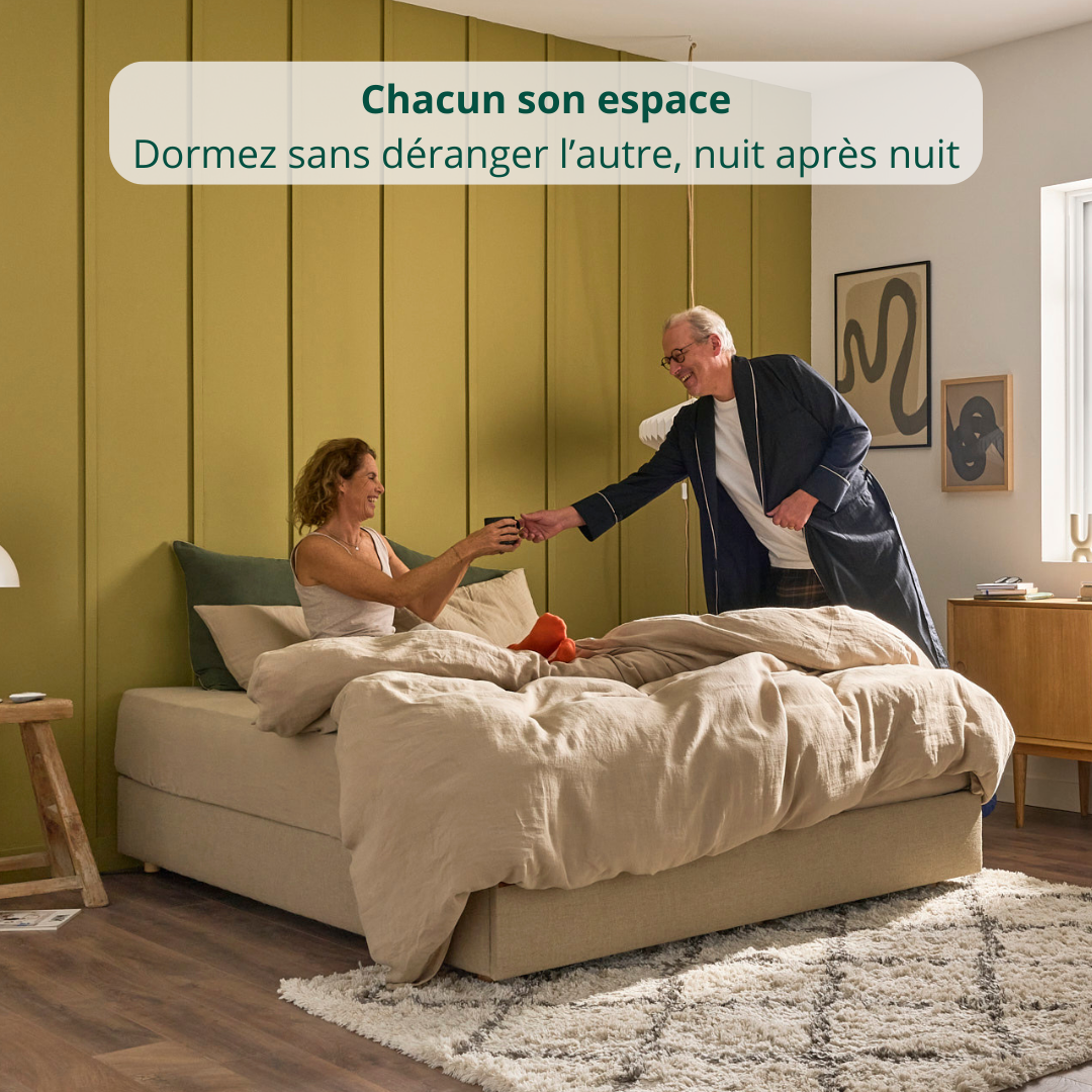 Un couple assis sur un matelas Merveilleux Bonnuit habillé d’une parure beige, adossé au mur avec bannière illustrant l'indépendance de couchage