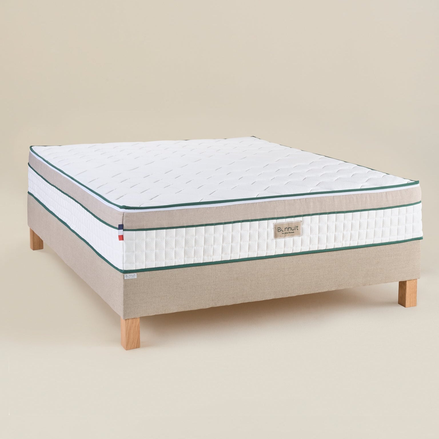 Matelas Le Merveilleux Bonnuit en ressorts ensachés et latex naturel, vue 3/4 avec bande en lin lavé, liseret vert, logo brodé et drapeau français
