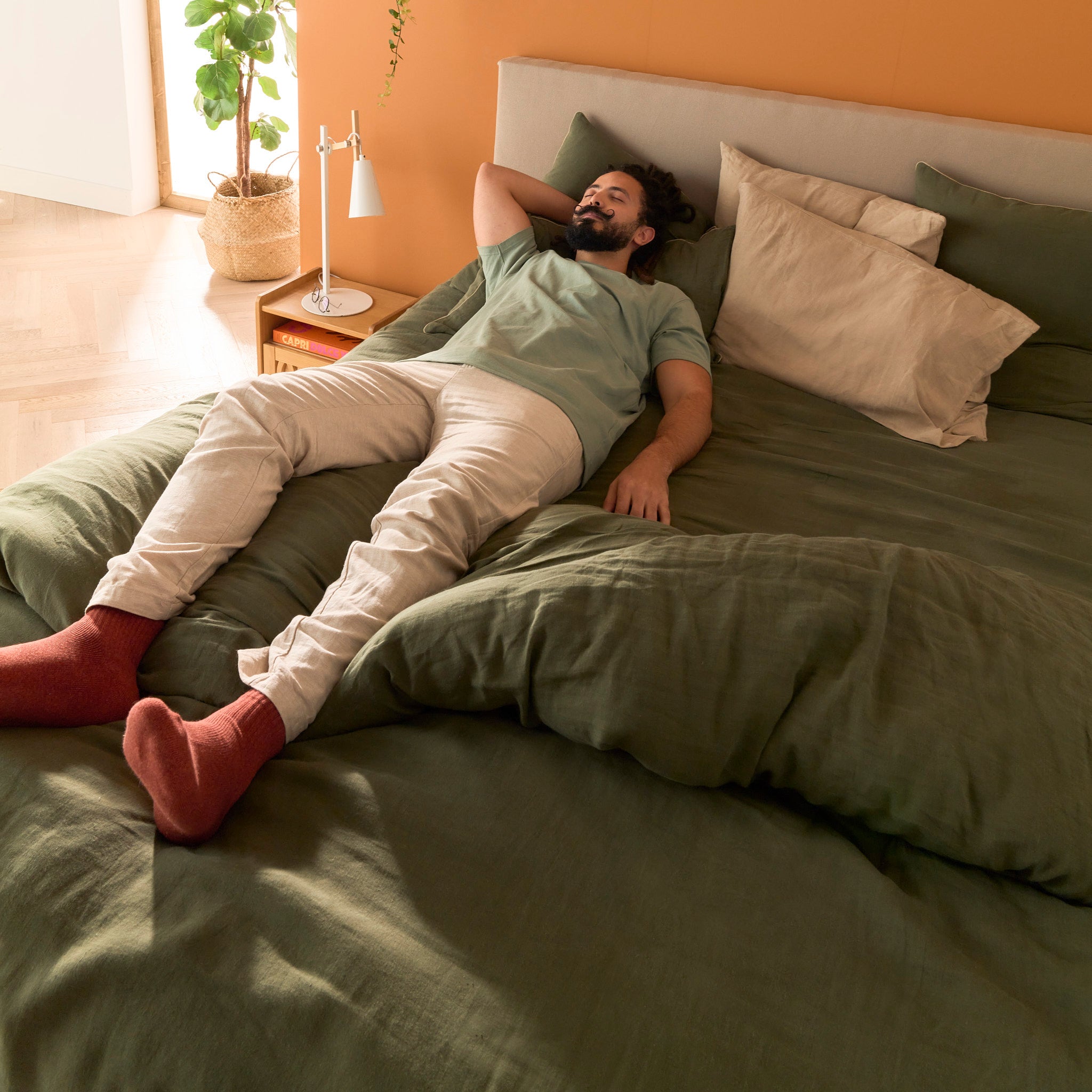 Homme allongé détendu sur le matelas Le Nuage Bonnuit habillé d’une parure en lin lavé kaki