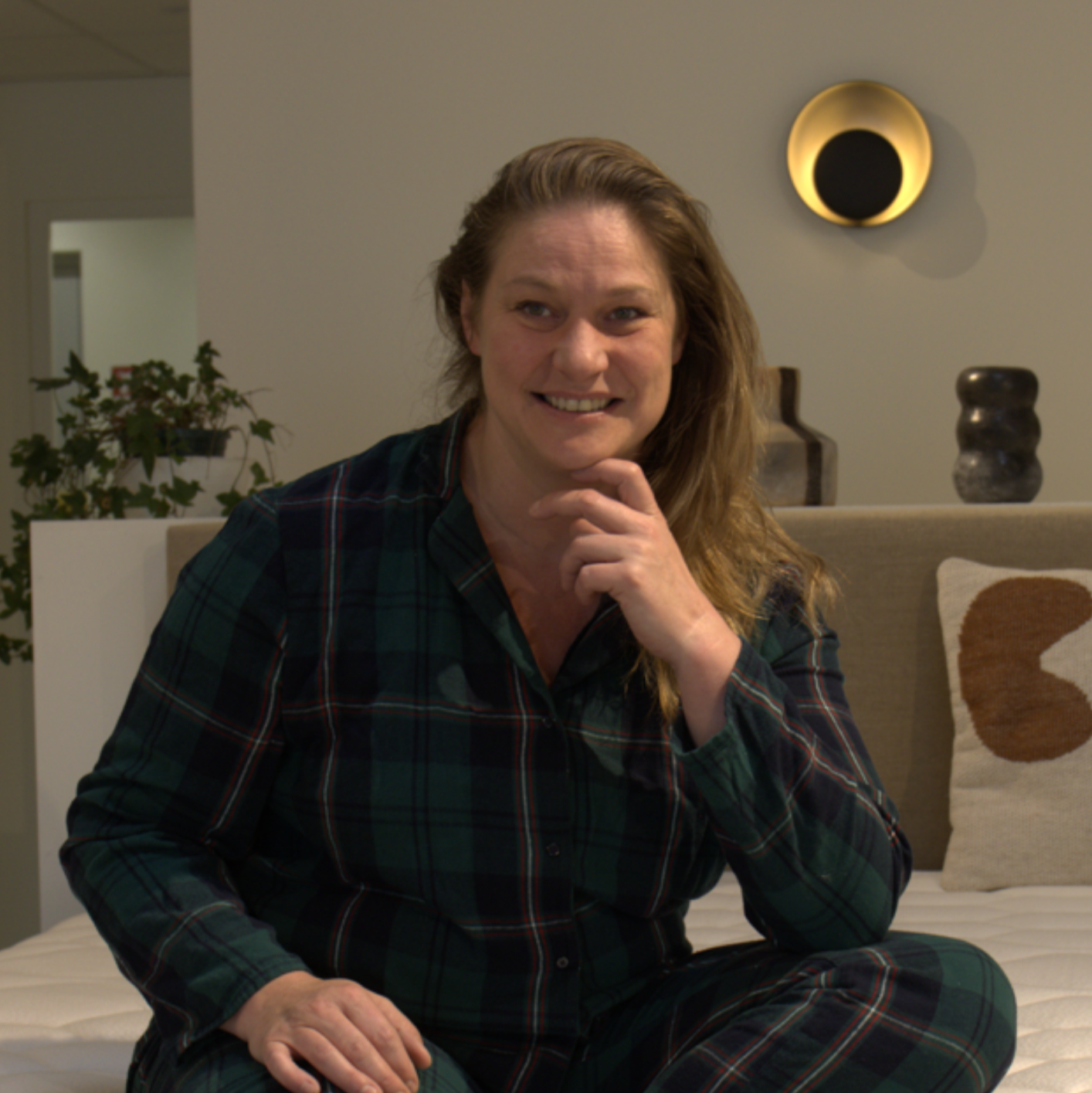 Portrait de la vendeuse du magasin Bonnuit à Bailleul, souriante et assise en pyjama sur un lit exposé