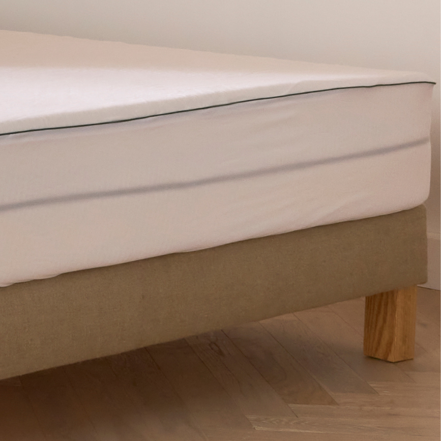 Zoom sur un protège-matelas Bonnuit avec côtés transparents, sommier en lin naturel et pied en bois visible