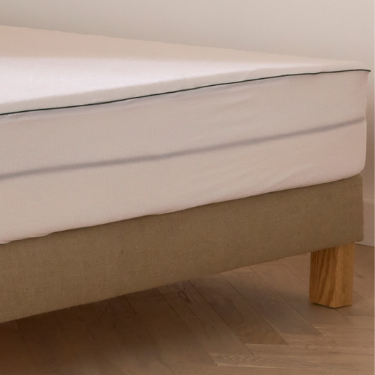 Zoom sur un protège-matelas Bonnuit avec côtés transparents, sommier en lin naturel et pied en bois visible