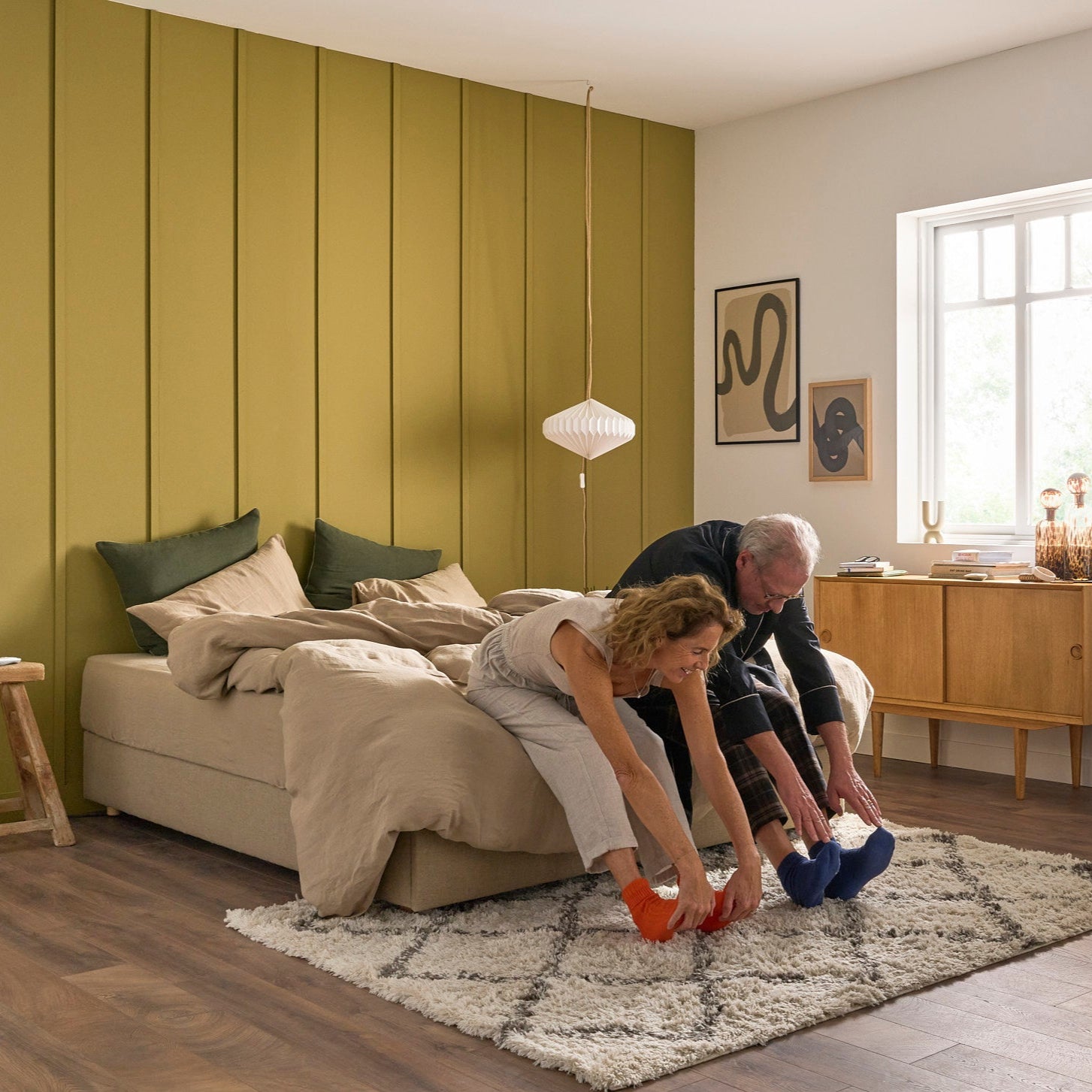 Couple assis au bout du lit sur le sommier Royal, linge en lin lavé beige, ambiance douce et complice