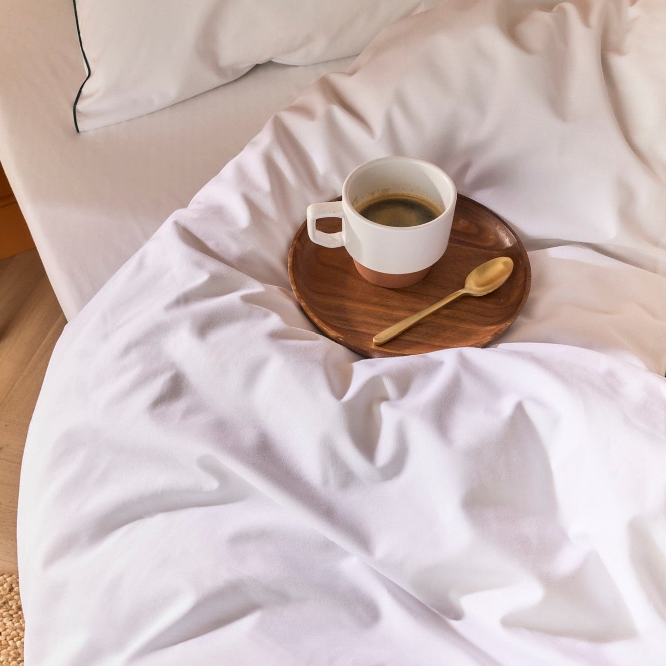 Tasse de café posée sur une couette habillée de linge de lit en percale blanche à liseré vert