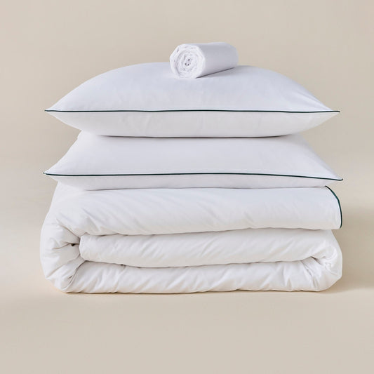 Parure de lit en percale de coton blanche avec liseré vert, oreillers posés sur la couette, drap roulé au-dessus