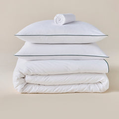 Parure de lit en percale de coton blanche avec liseré vert, oreillers posés sur la couette, drap roulé au-dessus