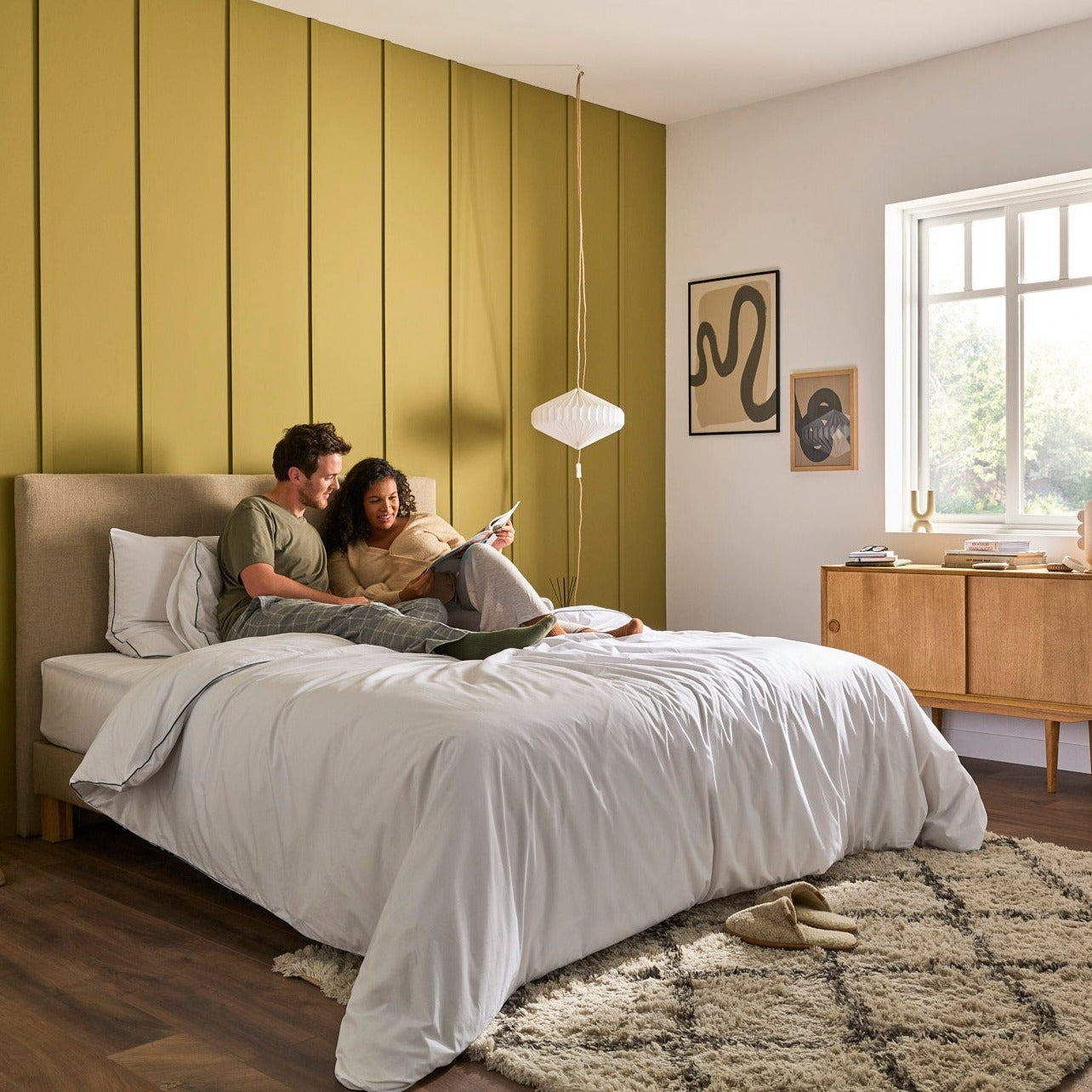 Couple lisant un livre sur la literie Bonnuit, sommier réglable, linge en percale blanche avec liseré vert
