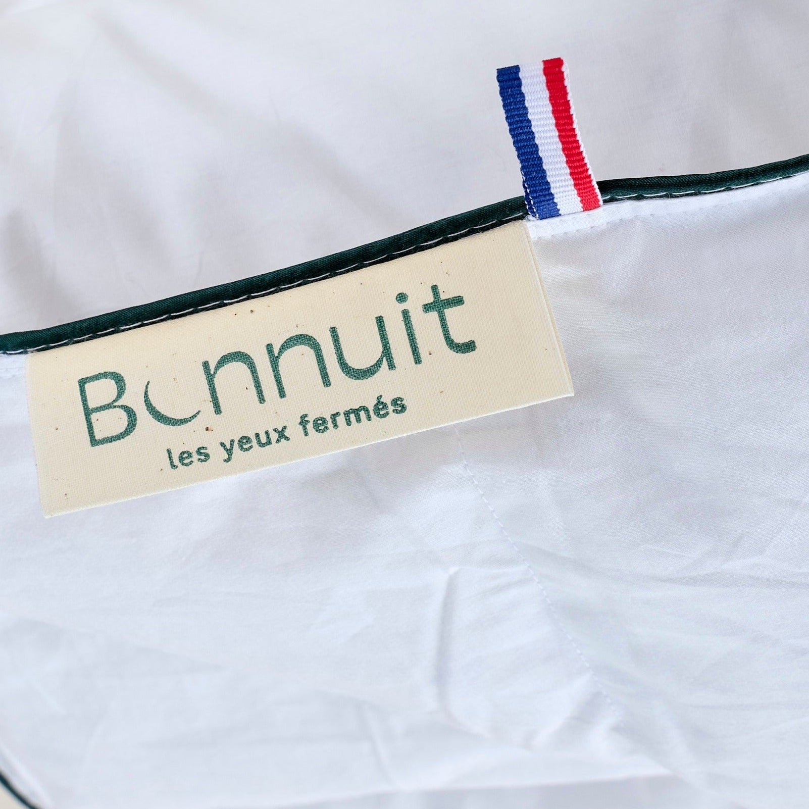 Zoom sur l’étiquette Bonnuit, le drapeau bleu blanc rouge et le liseré vert de la taie d’oreiller en percale blanche